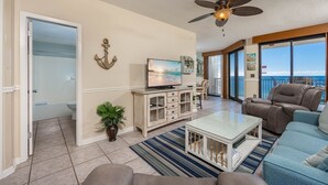 A spacious living room with a large window, a ceiling fan, and a view of the ocean. - Phoenix X 805 1 Bedroom Condo (Orange Beach)