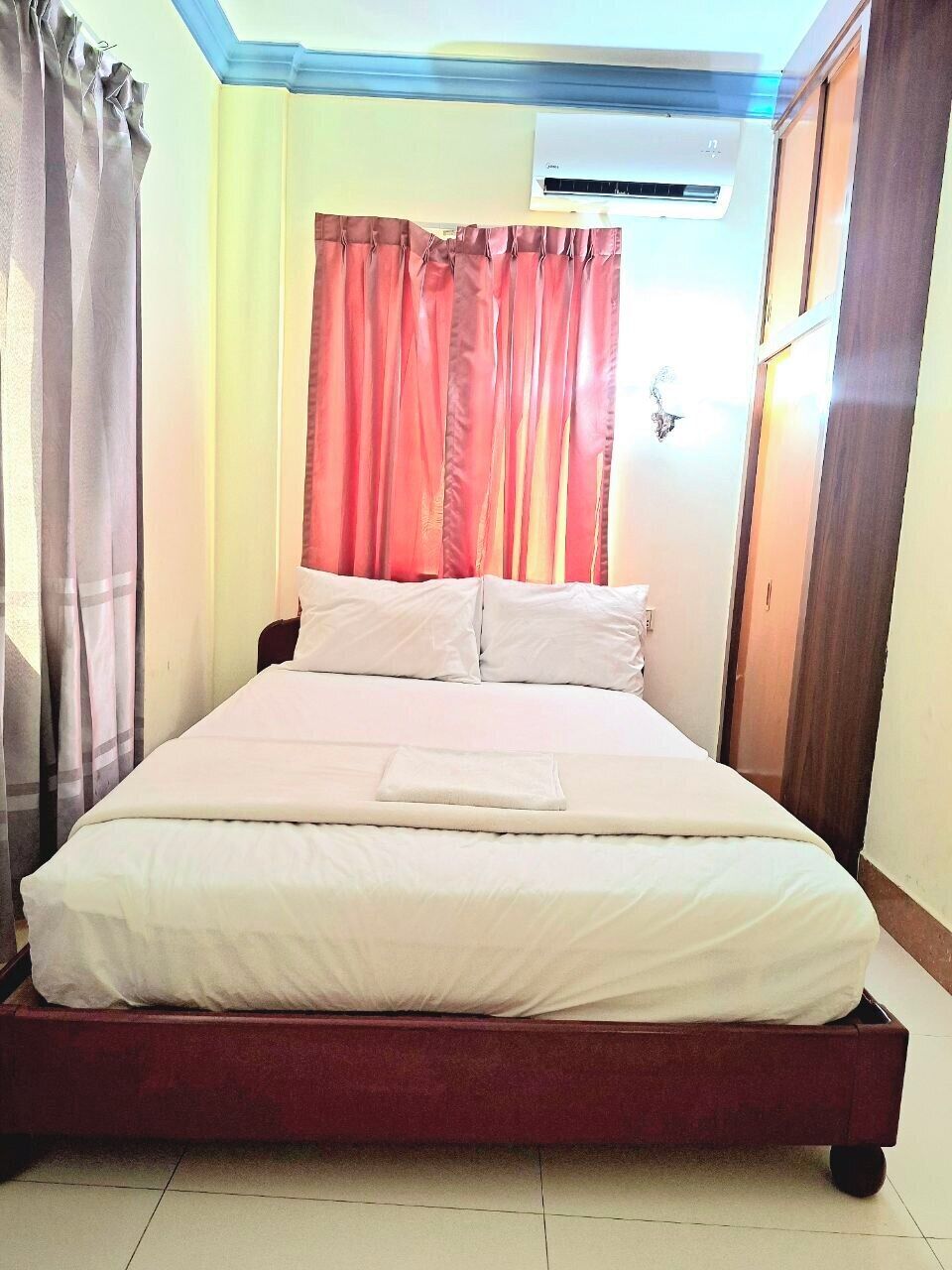 A bed with white bedding, a red headboard, and a window with red curtains.