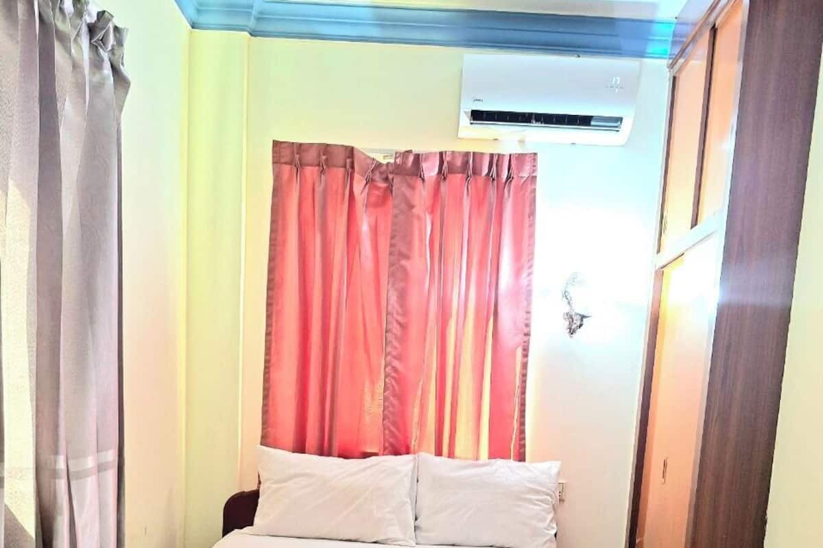 A bed with white bedding, a red headboard, and a window with red curtains.