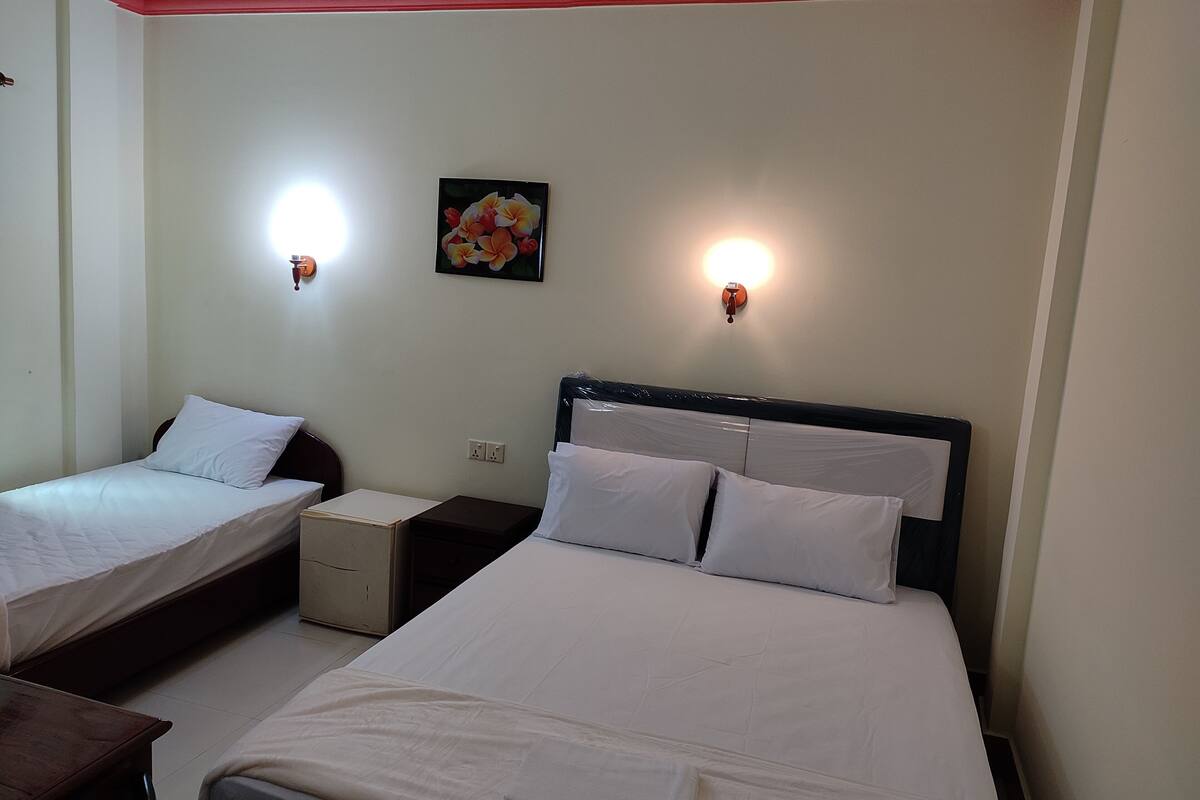 A hotel room with two single beds, a nightstand, a bedside table, a wall-mounted light, and a floral picture.