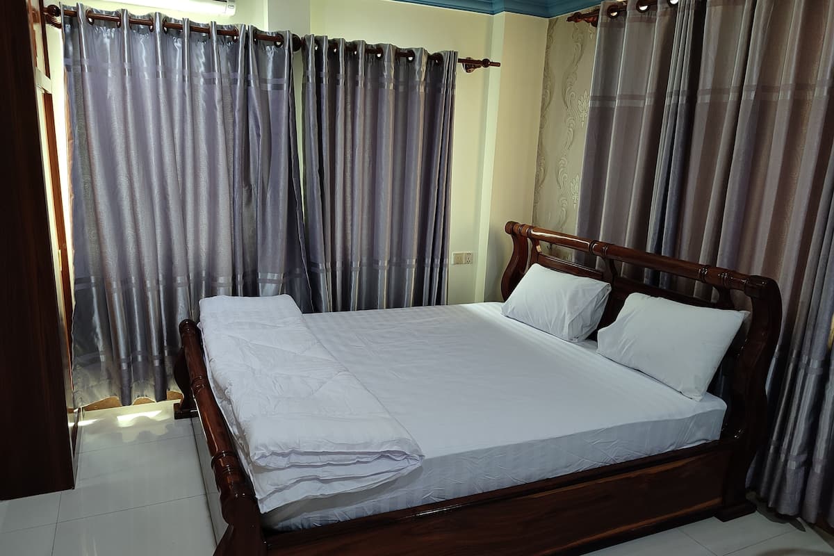 A neatly made bed with white linens in a room with wooden headboard and curtains.