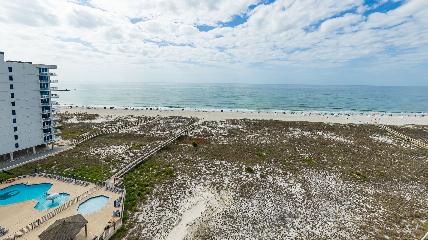 Un complejo turístico en la playa con piscina, zona de playa y un edificio con balcones.