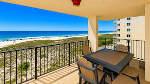 A balcony with a view of the beach, a table with chairs, and a red light fixture.