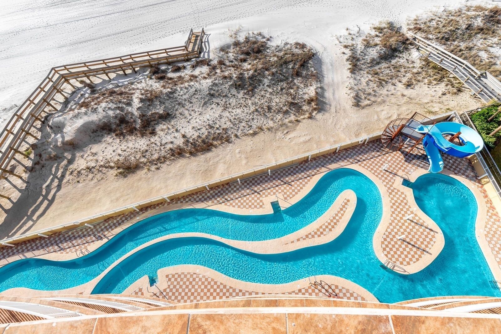 A swimming pool with a checkered pattern around the edges, a slide, and a deck area with a railing.