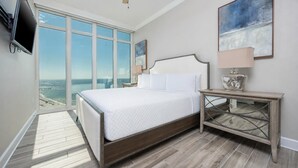 A bedroom with a large window, a bed, a nightstand, and a TV mounted on the wall. - Phoenix Orange Beach 2106 4 Bedroom Condo (Orange Beach)