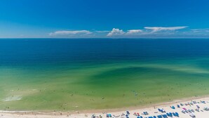 A beach with clear waters, a sandy shore, and umbrellas. - Phoenix Orange Beach 2106 4 Bedroom Condo (Orange Beach)