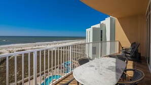 A balcony with a view of the beach, a pool, and a table with chairs. - Phoenix Orange Beach Ii 503 2 Bedroom Condo (Orange Beach)