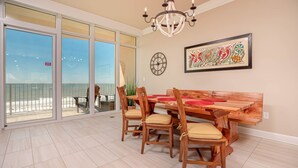 Ein Essbereich mit Holztisch und Stühlen, einer Kandelaber und einem großen Fenster mit Blick auf den Strand.
