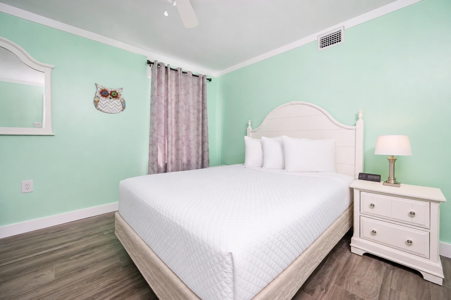 A bedroom with a bed, nightstand, lamp, and a wall-mounted mirror.