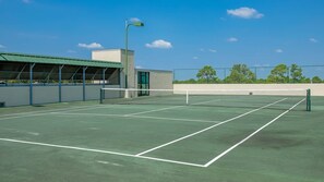 Un court de tennis extérieur, doté d’un filet, entouré d’une clôture et bordé d’un bâtiment dont le toit est végétalisé.