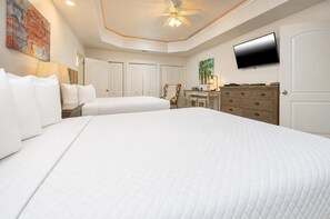 Une chambre d’hôtel avec un grand lit, un bureau, une chaise, une télévision et un ventilateur de plafond.