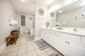 Une salle de bain moderne avec un grand miroir, des meubles blancs et un espace douche.