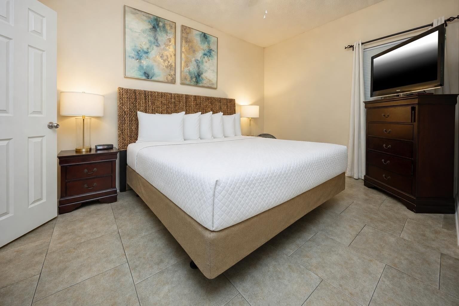 A hotel room with a large bed, two bedside lamps, a dresser, a TV, and abstract wall art.