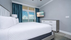 A bedroom with a bed, a dresser, a TV, and a window with curtains.