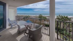 A balcony with wicker furniture, a small table, and a view of the beach.
