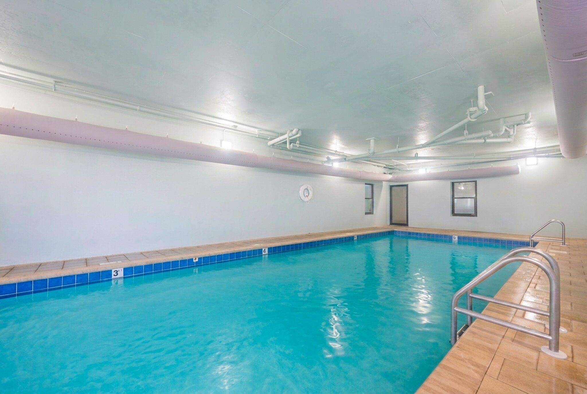 An indoor swimming pool with clear blue water, a tiled edge, and a wooden deck.