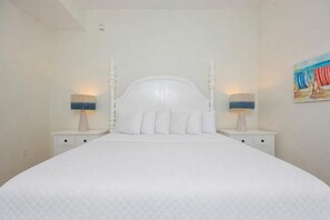 A large bed with a white headboard, two bedside tables with lamps, and a painting on the wall. - Phoenix Vii 7014 1 Bedroom Condo (Orange Beach)