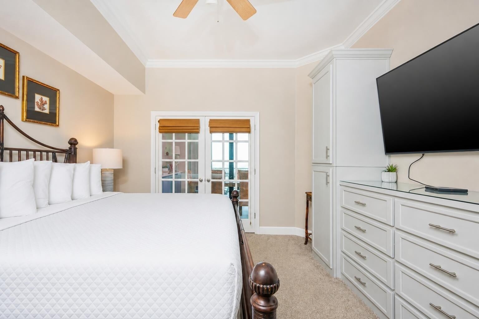 A hotel room with a bed, a television, a dresser, and a door leading to a balcony.