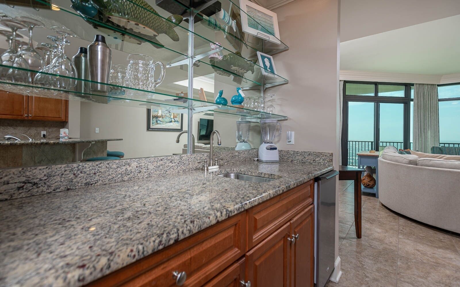 A modern kitchen with granite countertops, a built-in dishwasher, and a glass display shelf above the sink.