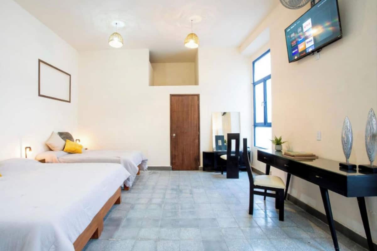 A hotel room with two beds, a desk, a chair, a TV, and a door.