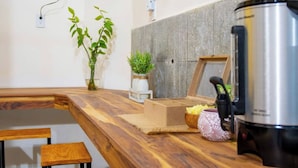 Eine Küche mit Holzarbeitsplatte, einem Edelstahl-Wasserkocher, einem kleinen Holzschemel und einem Blumentopf.