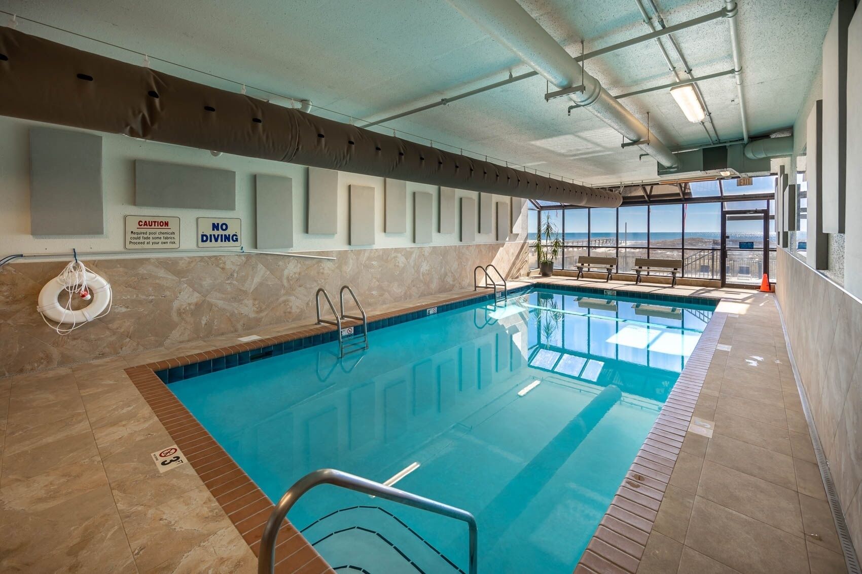 An indoor swimming pool with clear signage, a lifebuoy, and a view of the outside.