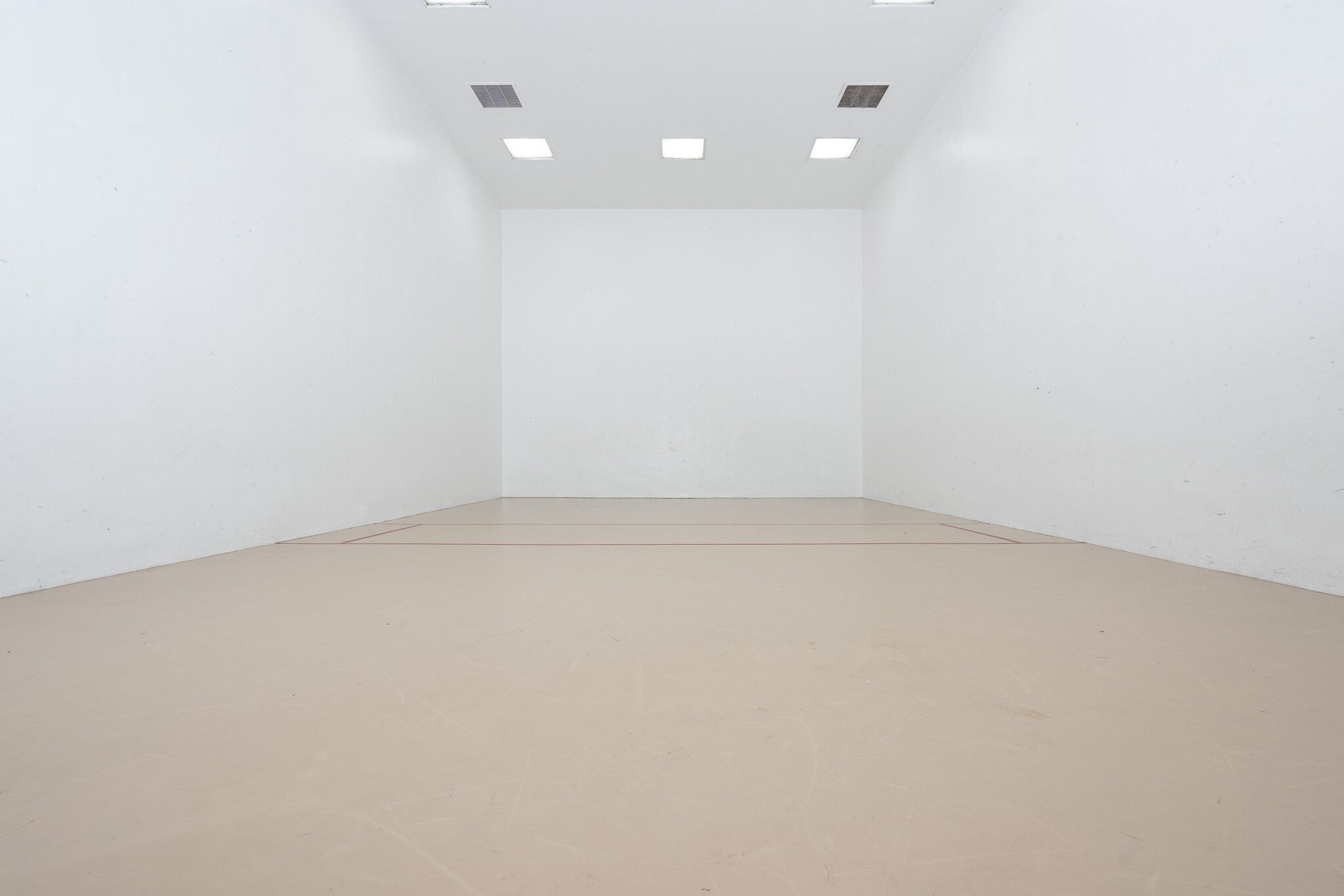 A clean, empty room with white walls and a beige floor, featuring recessed ceiling lights.