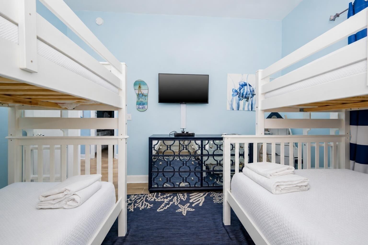 A room with bunk beds, a flat-screen TV, a desk with a computer, and a decorative wall piece.