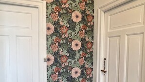 A hallway with a floral wallpaper, a wooden console table with a potted plant, and white double doors. - Sejerø Vandrerhjem (Sejero)
