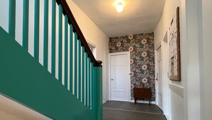 A hallway with teal stairs, a floral wallpaper, and a small wooden shelf. - Sejerø Vandrerhjem (Sejero)