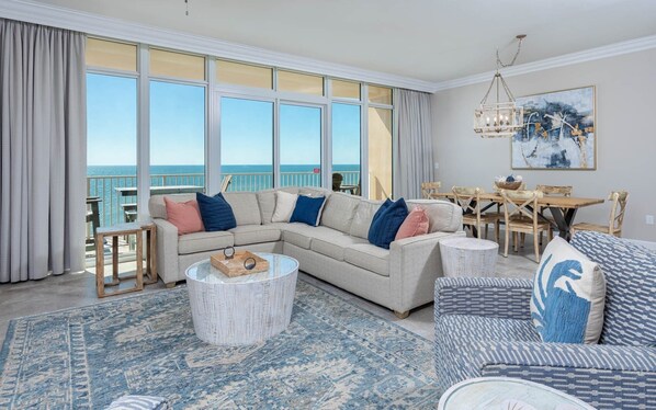A living room with a large sectional sofa, a round coffee table, and a dining area with wooden chairs and a table. - Phoenix Orange Beach Ii 1603 2 Bedroom Condo (Orange Beach)