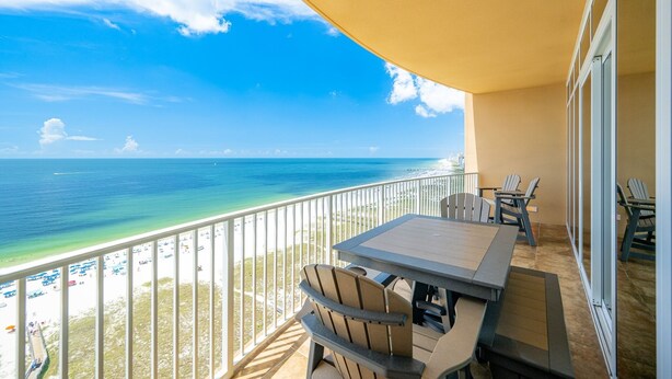 A balcony with a table and chairs overlooking a beach with a clear view of the ocean. - Phoenix Orange Beach Ii 1603 2 Bedroom Condo (Orange Beach)