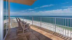 A balcony with a view of the beach and ocean, featuring a rocking chair and a tiled floor. - Phoenix Orange Beach Ii 1905 4 Bedroom Condo (Orange Beach)