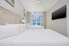 Habitación de hotel con una cama grande, ventilador de techo, televisión y vista al océano.