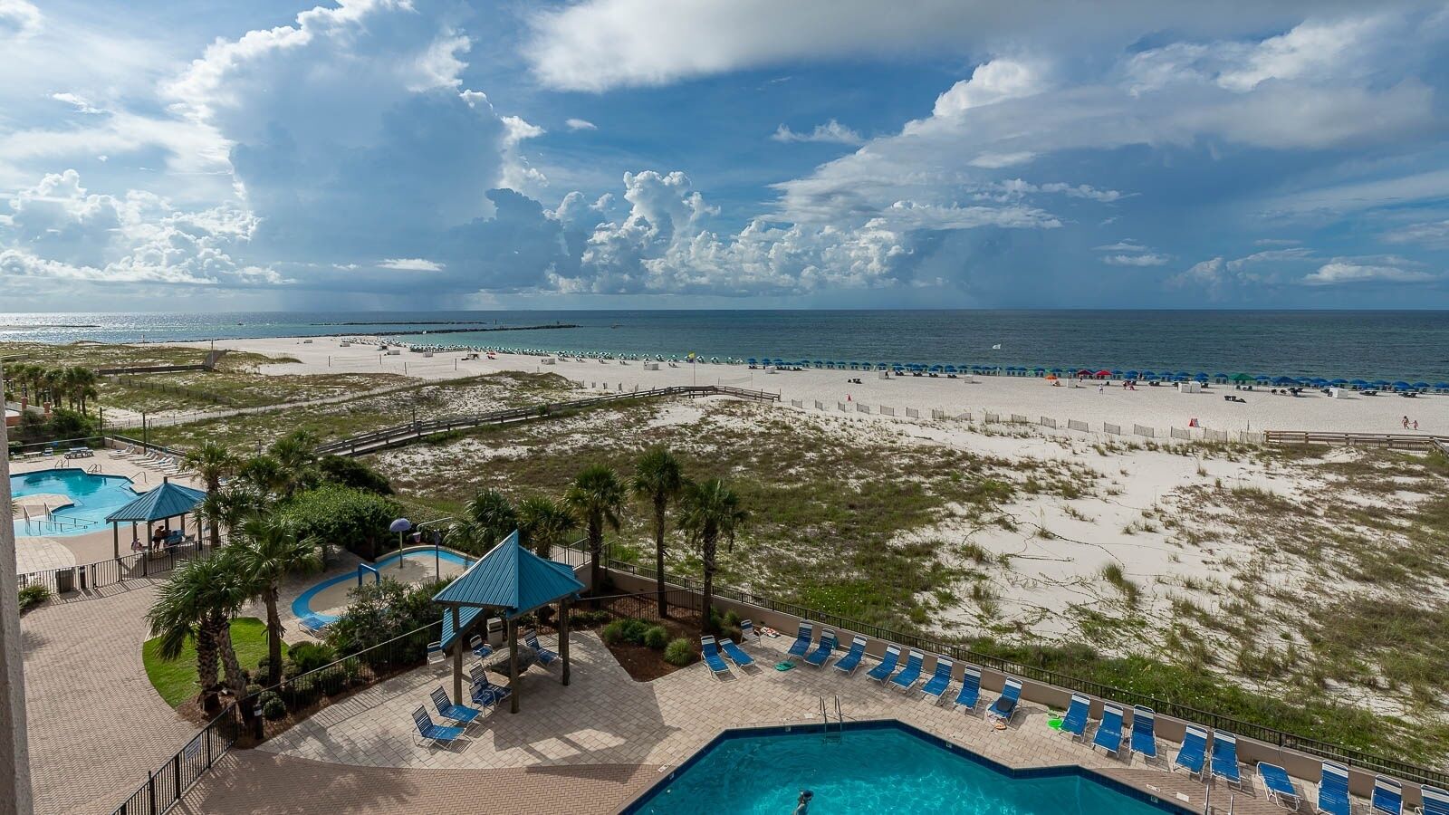 A beach resort with a swimming pool, lounge chairs, and a view of the ocean.