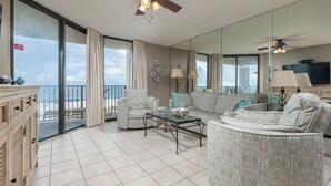 Un salon spacieux avec un grand canapé, des fauteuils, une table basse et un balcon offrant une vue sur la plage.