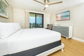 A bedroom with a bed, a ceiling fan, a dresser, a chair, and a view of the ocean.