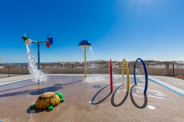 Un espacio de juegos acuáticos con una estructura con forma de tortuga, múltiples chorros de agua y una vista despejada de la playa al fondo.