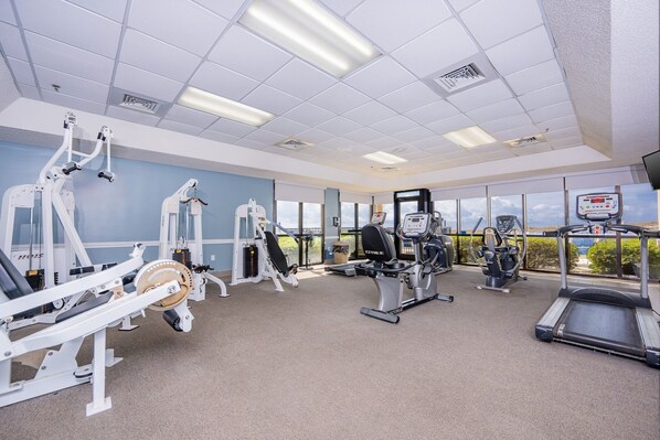 Un gimnasio con diverso equipamiento de ejercicio, amplias ventanas y vistas al exterior.