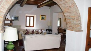 A cozy living room with a white sofa, a green lamp, and a brick fireplace archway.