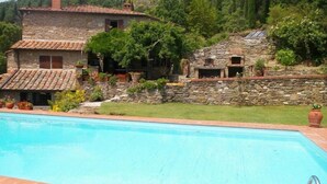 A stone house with a swimming pool, surrounded by greenery and hills.