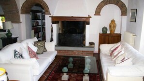 A living room with a fireplace, white sofas, a bookshelf, and a coffee table.