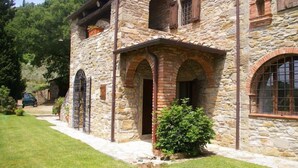 A stone building with arched doorways and windows, a small garden, and a car parked outside.