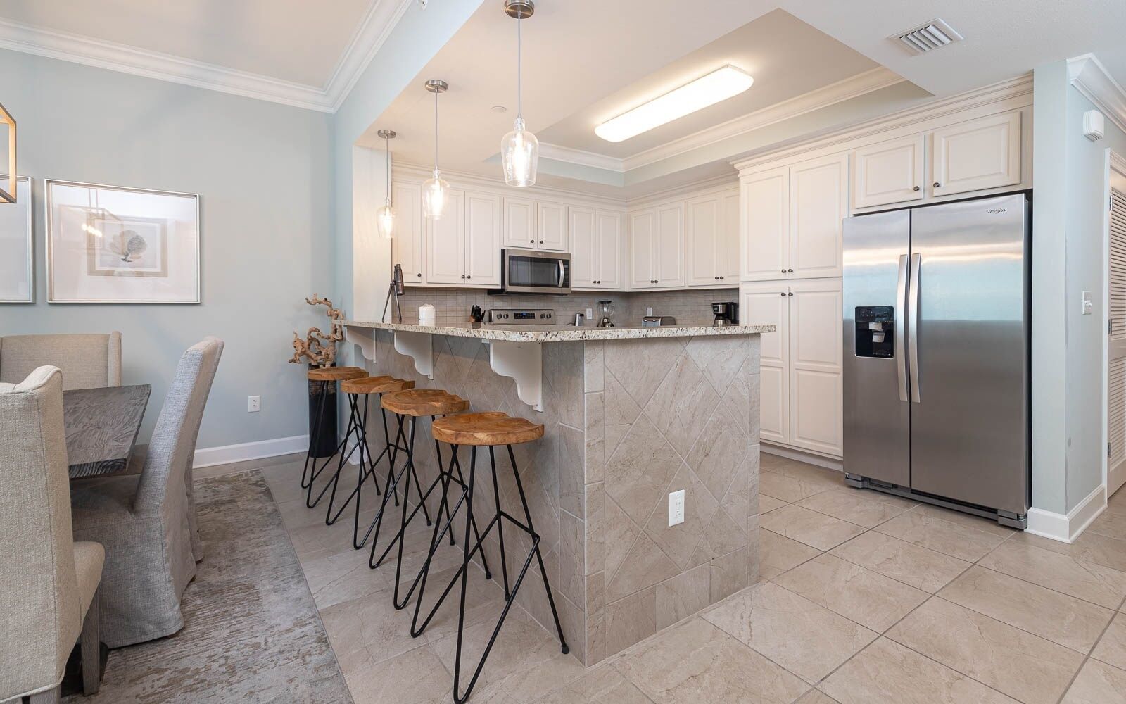 A kitchen with a central island, bar stools, a refrigerator, and pendant lighting.