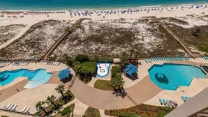 An aerial view of a beach resort with multiple swimming pools, sun loungers, and a sandy beach area. - Phoenix East 1111 3 Bedroom Condo (Orange Beach)