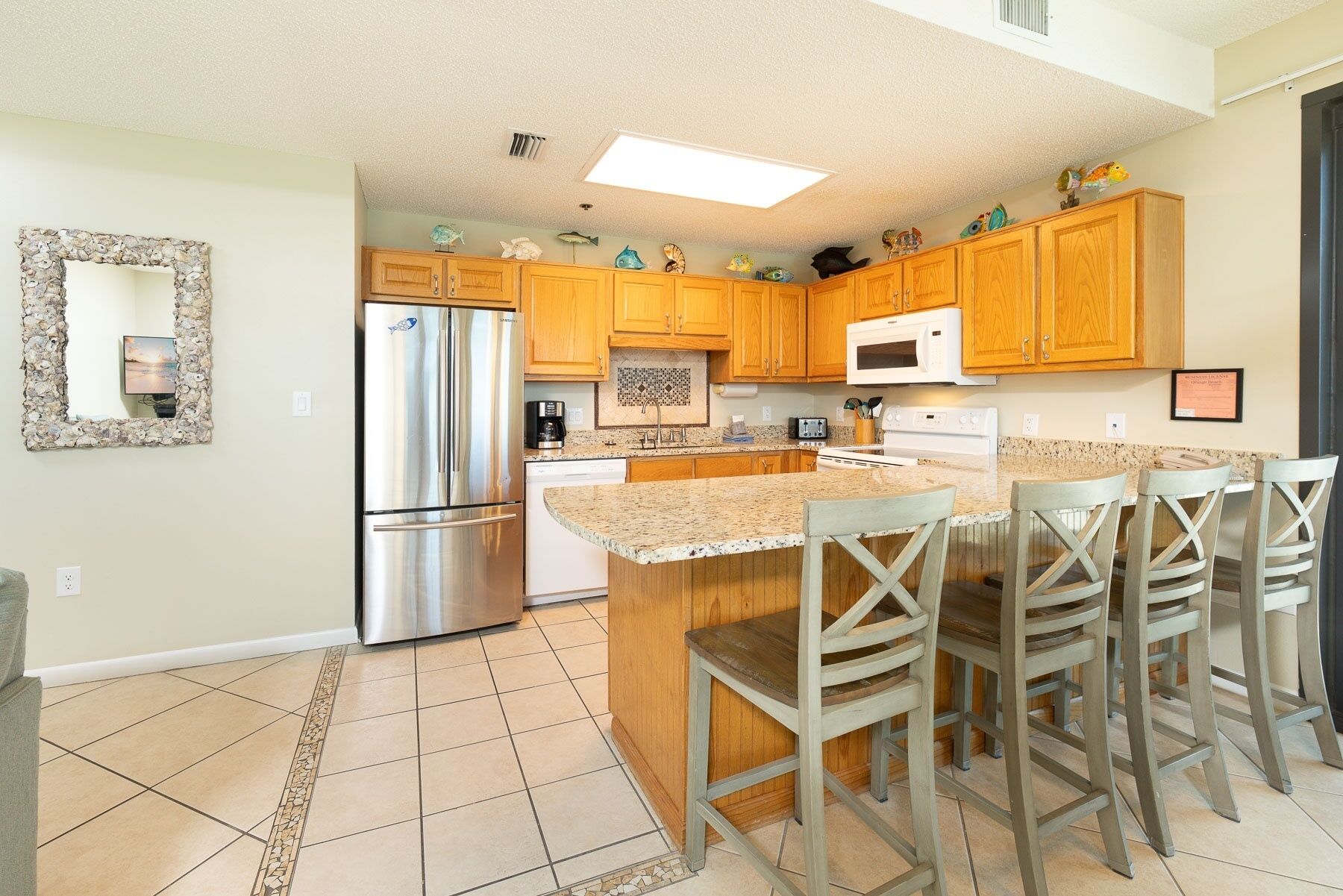 A kitchen with wooden cabinets, a stainless steel refrigerator, a microwave, and a tiled floor.