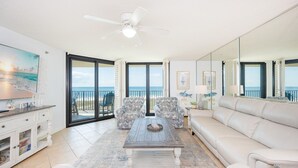 A spacious living room with a large window, a ceiling fan, and a view of the ocean. - Phoenix Vii 7503 3 Bedroom Condo (Orange Beach)