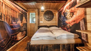 Een rustieke houten kamer met een bed, houten wanden en een grote muurschildering van een hand die druiven vasthoudt.