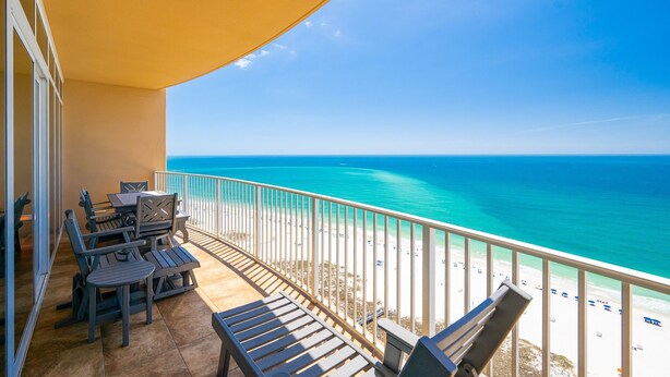 A balcony with outdoor furniture overlooking a beach.