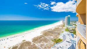 A beach with a clear sky, a sandy shore, and a high-rise building with balconies overlooking the beach.